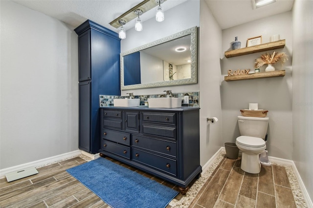 bathroom with baseboards, wood tiled floor, double vanity, a sink, and toilet