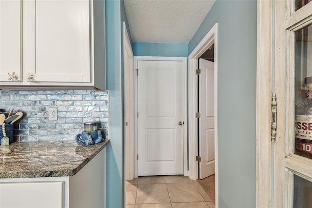 kitchen with white cabinetry, dark stone counters, decorative backsplash, light tile patterned flooring, and a textured ceiling