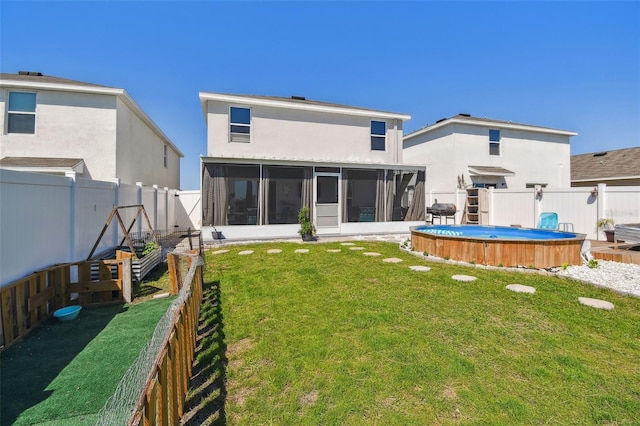 back of house with a fenced in pool, a sunroom, stucco siding, a yard, and a fenced backyard