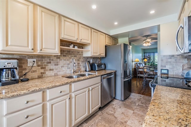 kitchen with light stone counters, a sink, ceiling fan, stainless steel appliances, and backsplash