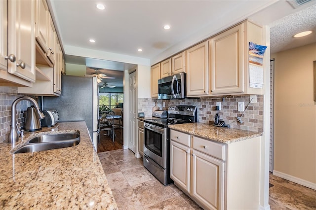 kitchen with baseboards, ceiling fan, cream cabinetry, stainless steel appliances, and a sink