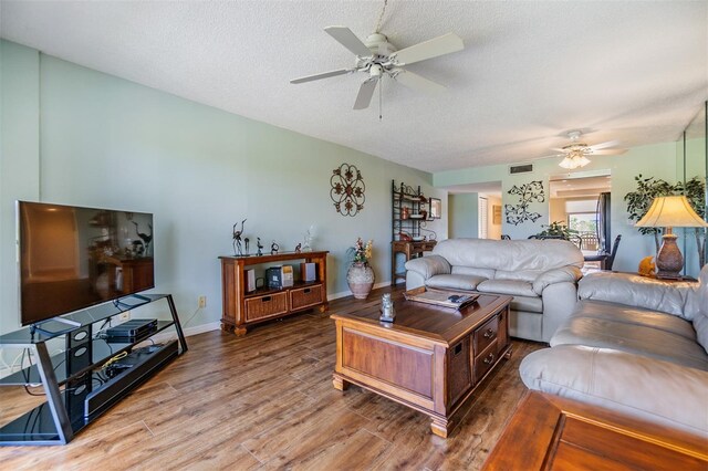 living area featuring visible vents, baseboards, wood finished floors, a textured ceiling, and a ceiling fan