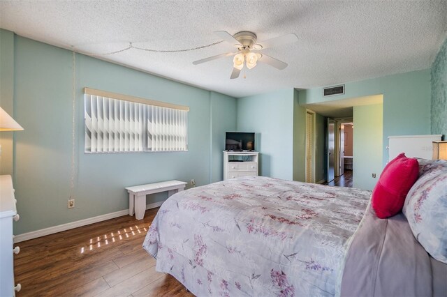 bedroom featuring wood finished floors, visible vents, baseboards, ceiling fan, and a textured ceiling