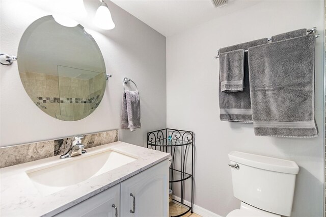 bathroom with tiled shower, toilet, vanity, and baseboards