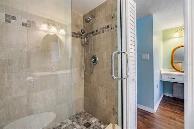 full bath featuring a shower stall, wood finished floors, baseboards, and a textured ceiling