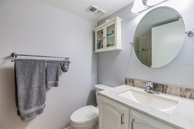 bathroom with a shower with shower door, visible vents, toilet, and vanity