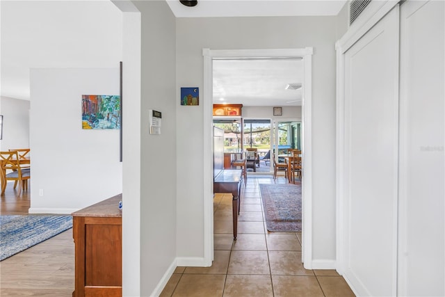 hall featuring light tile patterned floors, visible vents, and baseboards