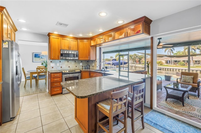 kitchen with dark stone countertops, a sink, decorative backsplash, appliances with stainless steel finishes, and brown cabinets