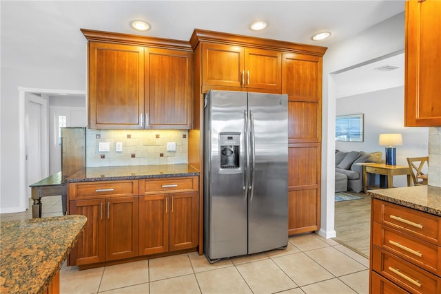 kitchen featuring tasteful backsplash, dark stone countertops, brown cabinetry, and stainless steel refrigerator with ice dispenser