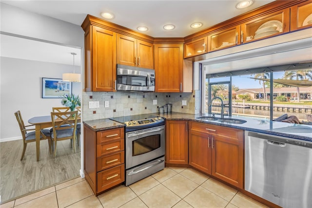 kitchen featuring brown cabinetry, dark stone countertops, appliances with stainless steel finishes, and a sink