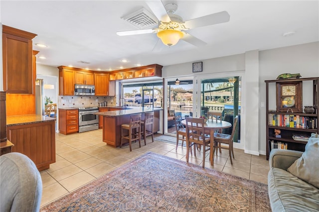 kitchen featuring visible vents, a ceiling fan, a sink, a kitchen breakfast bar, and appliances with stainless steel finishes