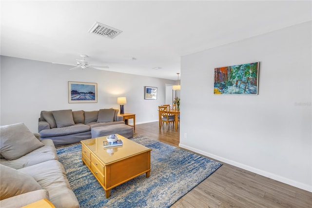 living area with baseboards, wood finished floors, visible vents, and ceiling fan