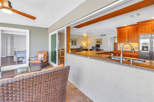 kitchen with visible vents, stainless steel fridge with ice dispenser, stone counters, a ceiling fan, and a sink