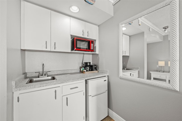 kitchen featuring light countertops, white cabinets, freestanding refrigerator, and a sink