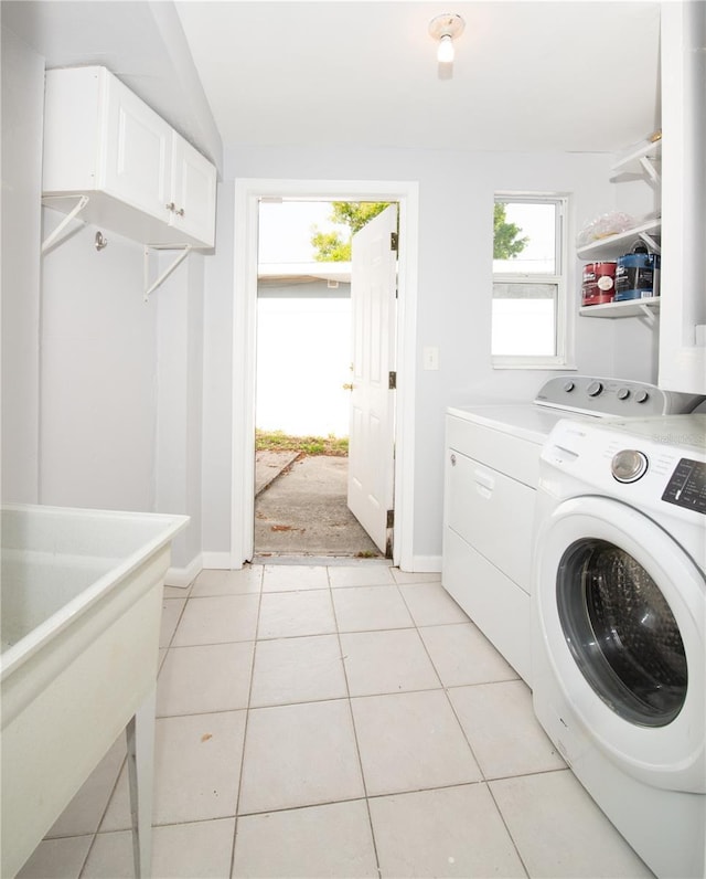 clothes washing area with a sink, washing machine and clothes dryer, light tile patterned floors, baseboards, and cabinet space