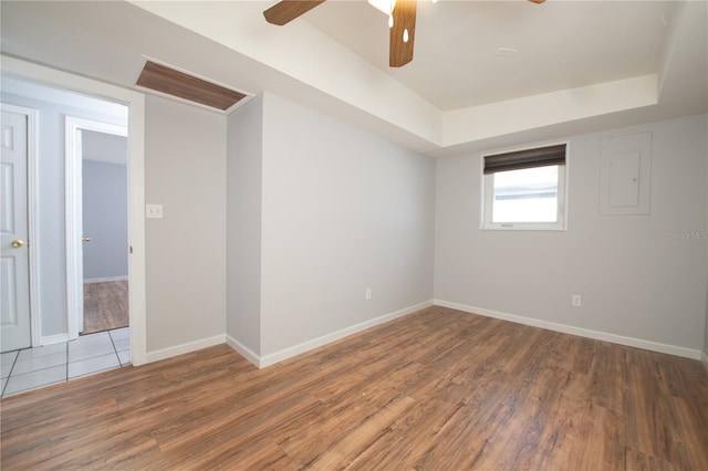 spare room with baseboards, wood finished floors, a raised ceiling, and a ceiling fan
