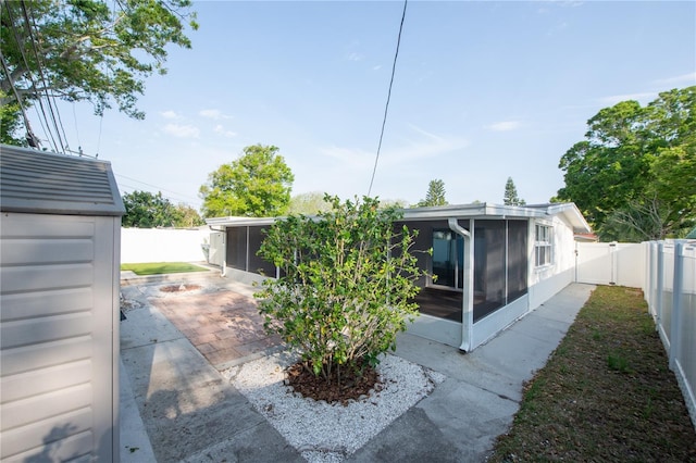rear view of house with a fenced backyard, an outdoor structure, a sunroom, and a patio