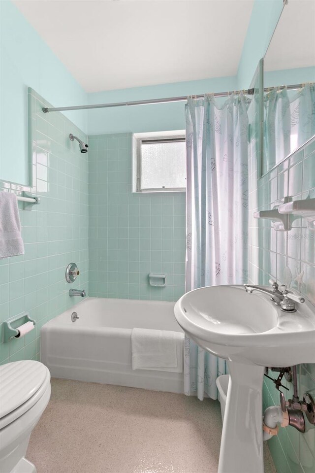 bathroom with toilet, shower / tub combo with curtain, speckled floor, and tile walls