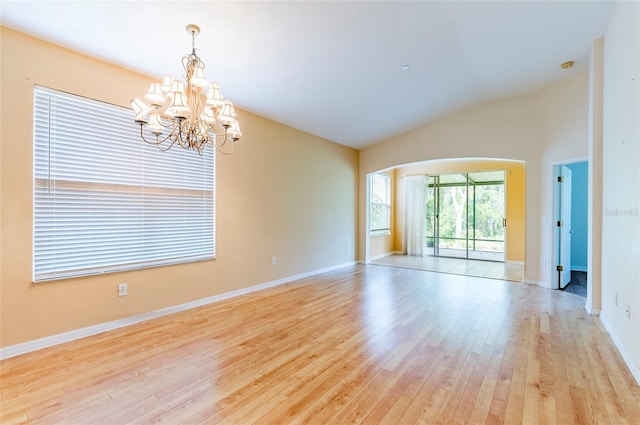 spare room with lofted ceiling, an inviting chandelier, baseboards, arched walkways, and light wood-style flooring