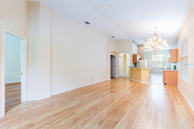 unfurnished living room featuring light wood-type flooring, baseboards, visible vents, arched walkways, and an inviting chandelier