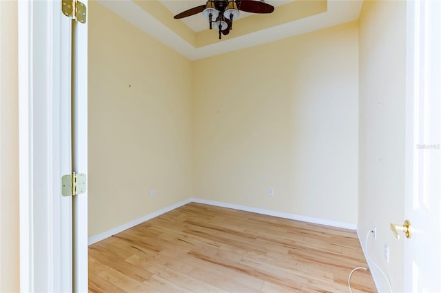 spare room featuring baseboards, a tray ceiling, wood finished floors, and a ceiling fan