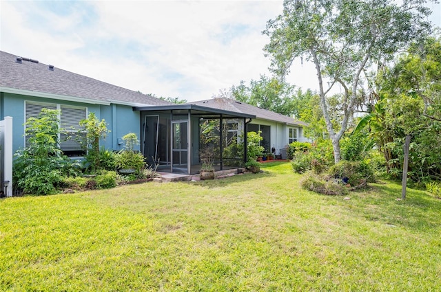back of property featuring a shingled roof, a sunroom, stucco siding, and a lawn