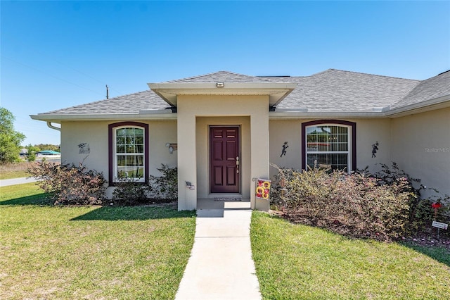 entrance to property with stucco siding, a lawn, and a shingled roof