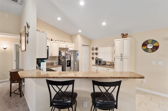 kitchen with light stone counters, a peninsula, lofted ceiling, a kitchen bar, and stainless steel fridge