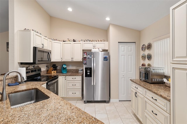 kitchen featuring light stone countertops, light tile patterned flooring, a sink, vaulted ceiling, and appliances with stainless steel finishes