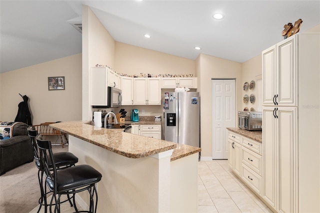 kitchen with a breakfast bar area, light stone countertops, a peninsula, stainless steel appliances, and vaulted ceiling
