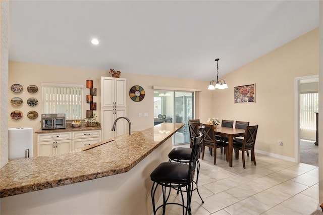 kitchen featuring light stone countertops, lofted ceiling, a sink, pendant lighting, and a notable chandelier