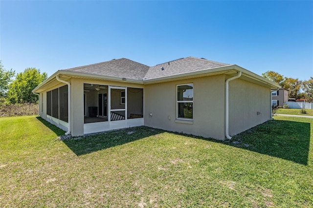 back of property with a sunroom, a yard, roof with shingles, and stucco siding