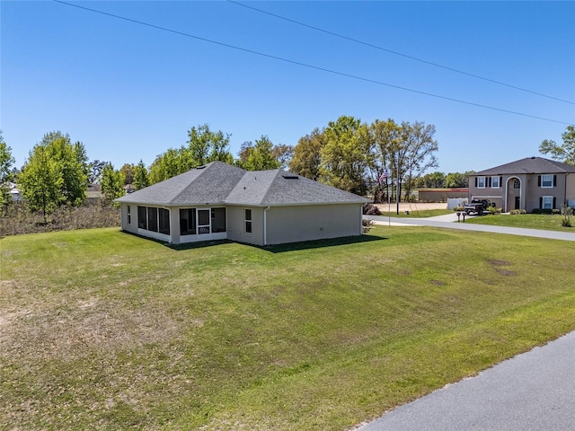 rear view of house with stucco siding, a lawn, driveway, and a sunroom