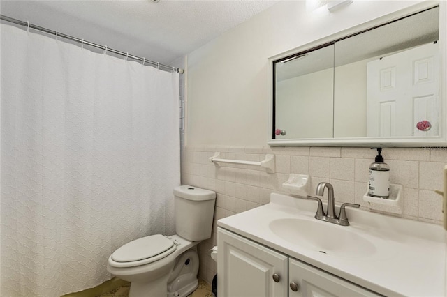 full bath with a wainscoted wall, toilet, vanity, a textured ceiling, and tile walls