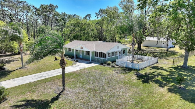 view of front of house featuring concrete driveway, fence, a front lawn, and a sunroom