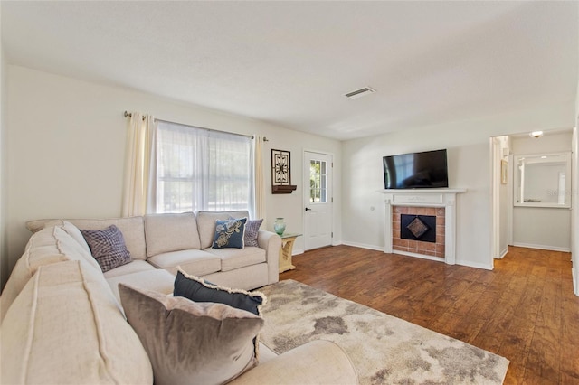 living room with visible vents, baseboards, wood finished floors, and a tile fireplace