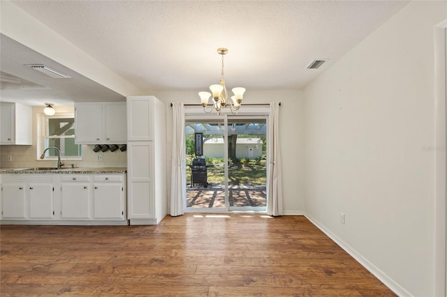 unfurnished dining area with visible vents, a sink, dark wood-style floors, baseboards, and a chandelier