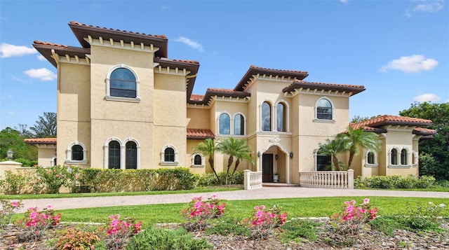 mediterranean / spanish-style home featuring stucco siding, curved driveway, a front lawn, and a tiled roof