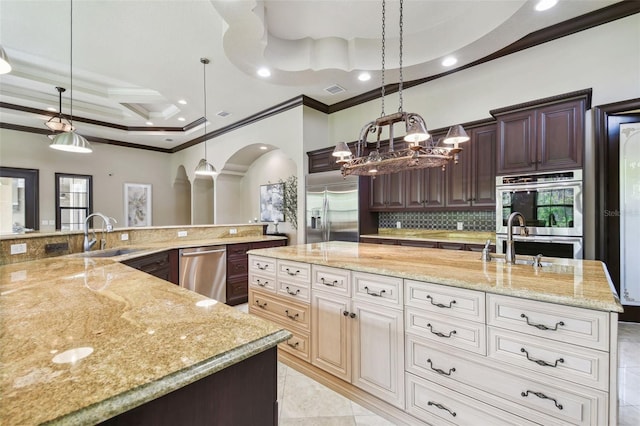 kitchen with a large island, a sink, arched walkways, appliances with stainless steel finishes, and light stone countertops