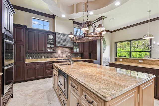 kitchen featuring a center island with sink, ornamental molding, decorative backsplash, a sink, and a chandelier