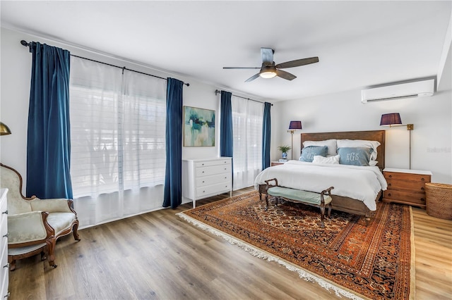 bedroom with a wall unit AC, ceiling fan, and wood finished floors