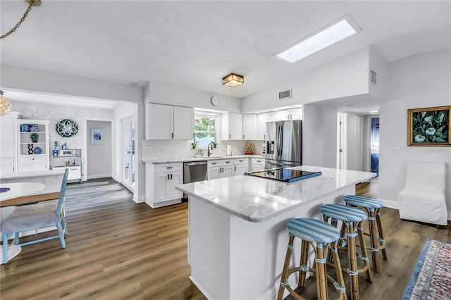 kitchen with dark wood-style flooring, a breakfast bar, vaulted ceiling with skylight, white cabinets, and appliances with stainless steel finishes