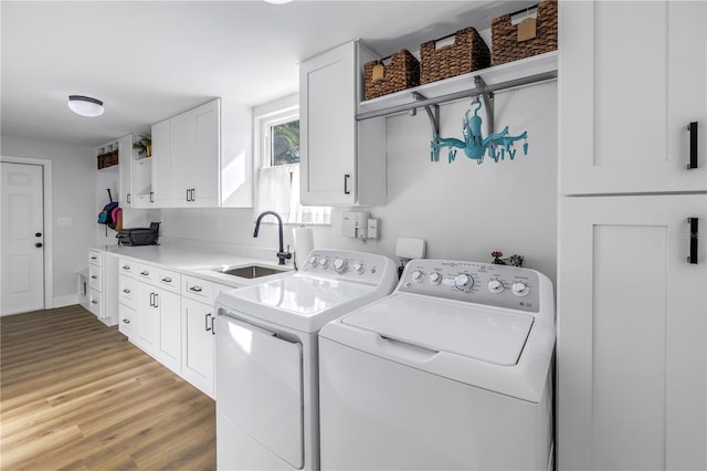 clothes washing area with light wood finished floors, separate washer and dryer, cabinet space, and a sink