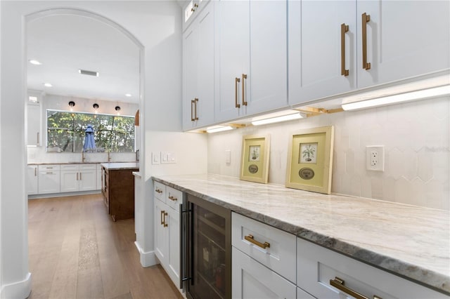bar featuring backsplash, beverage cooler, recessed lighting, light wood-style flooring, and arched walkways