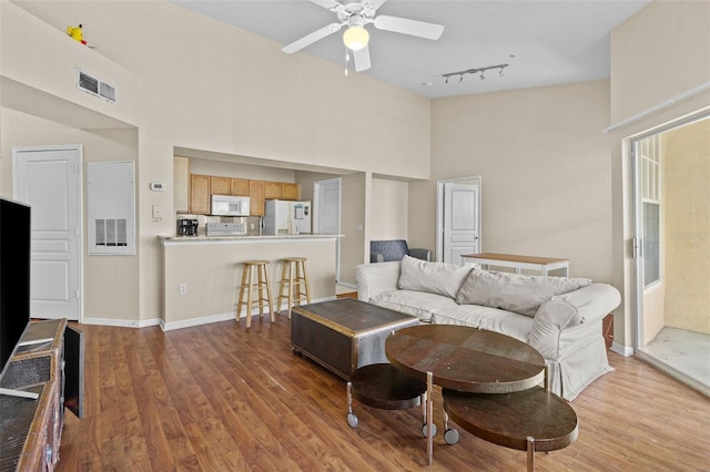 living room featuring visible vents, a ceiling fan, wood finished floors, baseboards, and a towering ceiling