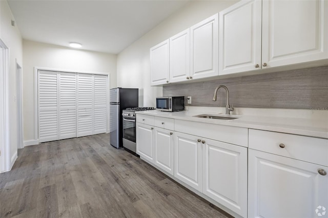 kitchen with white cabinetry, light countertops, light wood-type flooring, a sink, and appliances with stainless steel finishes