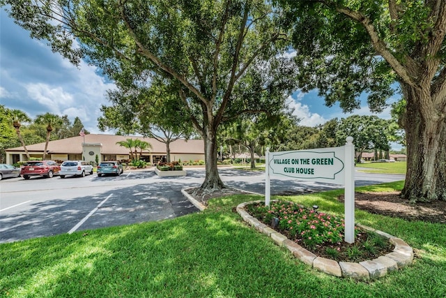 community sign featuring a lawn and uncovered parking