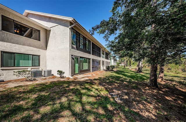 rear view of house with stucco siding, central AC unit, and a yard