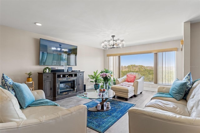 living area featuring wood finished floors, a glass covered fireplace, baseboards, recessed lighting, and an inviting chandelier