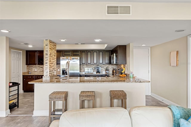 kitchen with dark brown cabinetry, visible vents, stainless steel appliances, and light stone counters